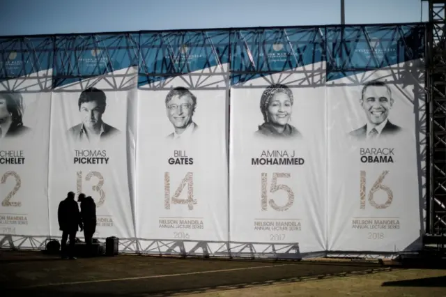 People stand near a banner depicting former US president Barak Obama (R) and other annual speakers prior to his speech for the 2018 Nelson Mandela Annual Lecture outside the Wanderers cricket stadium in Johannesburg on July 17, 2018.