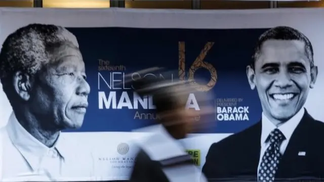 A person walks past a banner depicting former South African leader Nelson Mandela (L) and former US president Barak Obama outside the Wanderers cricket stadium in Johannesburg on July 17, 2018