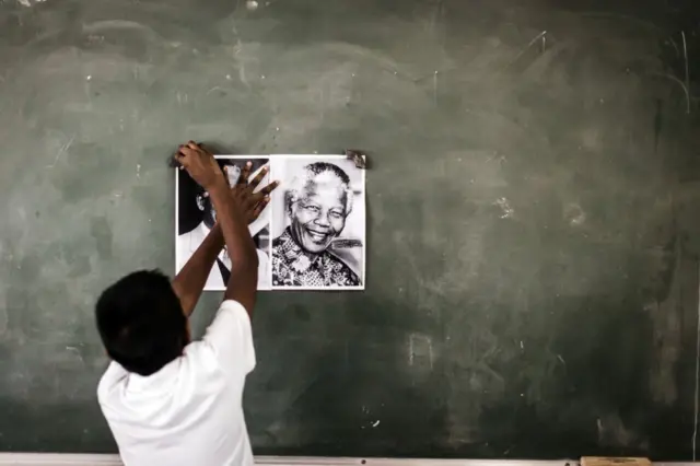 A child from Northlen Primary school sticks a poster of former South African President Nelson Mandela on the chalkboard in Durban on 18 July 2018