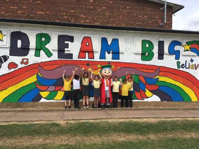 A line of pupils with their arms up standing in front of their Dream Big mural