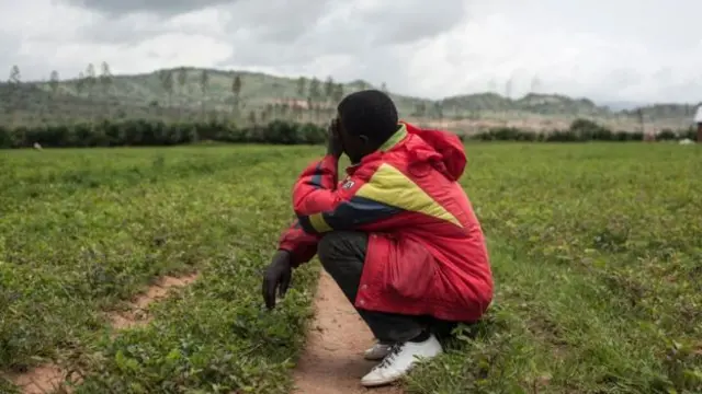 A man crouches down in a field with one hand covering his face in grief