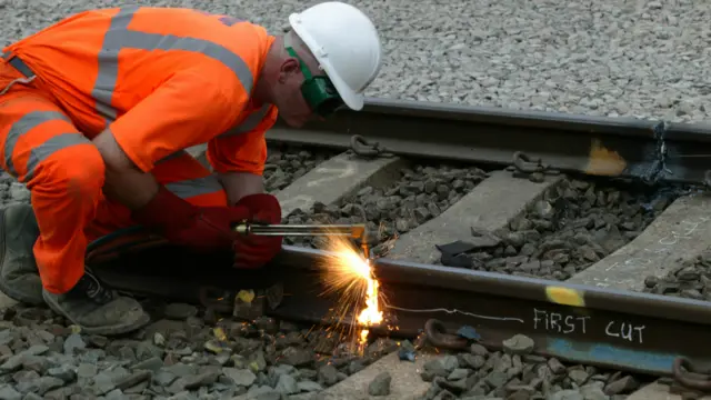 A man wearing a white hard hat and orange overalls working on a railway line