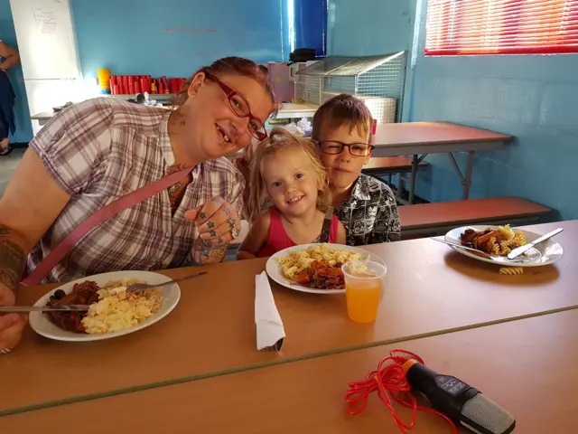 Mother of two on the breadline enjoying free cooked meal with her children.