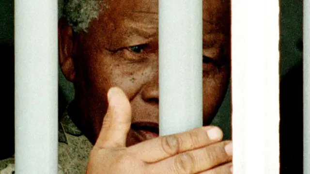 Nelson Mandela stands on 27 March1998 behind the bars of the former cell where he spent 18 of his 27 years as a political prisoner on Robben Island