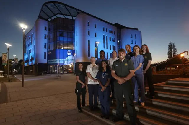 Students stand in front of the blue lit Allam Medical Building