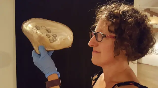 Curator Rebecca Machin holds pearl Buddha figures made inside an oyster shell.