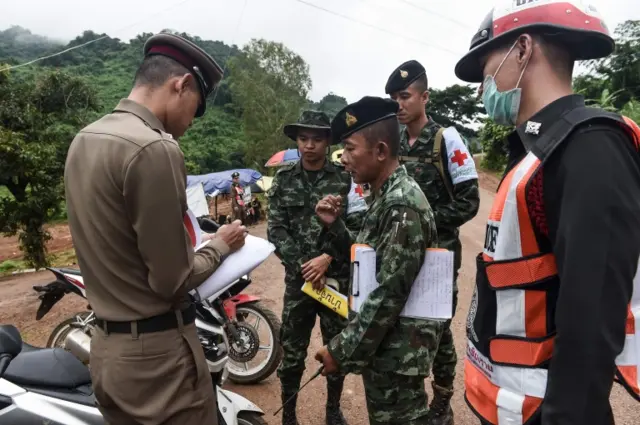 A Thai police officer and soldiers discuss the rescue operation