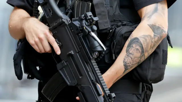 An armed police officer with tattoos on show