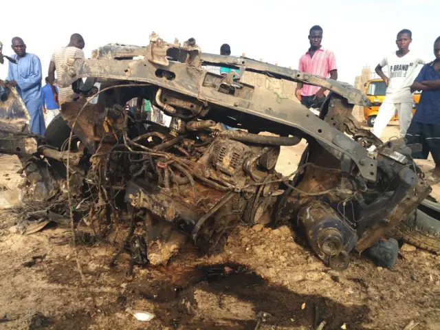 People look at a vehicle destroyed by the military during cross fire with Boko Haram Islamists which killed at least four, in Maiduguri, on April 27, 2018