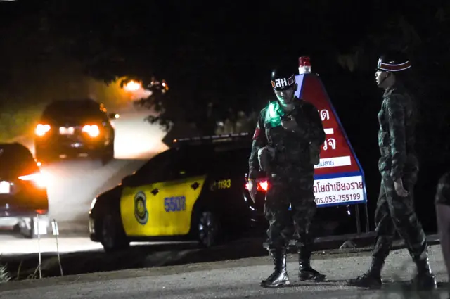 Military police secure the road for a large convoy of official vehicles entering the Tham Luang cave area