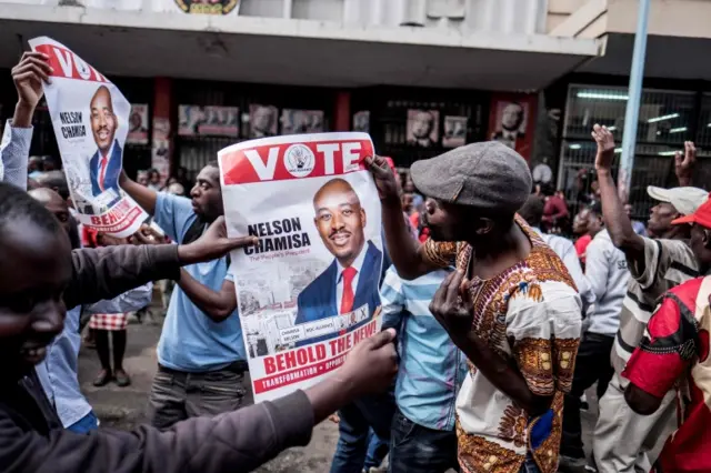 Supporters of Zimbabwean opposition MDC Alliance party leader Nelson Chamisa hold his campaign posters as they gather outside the MDC Alliance"s headquarters in Harare on July 31, 2018.