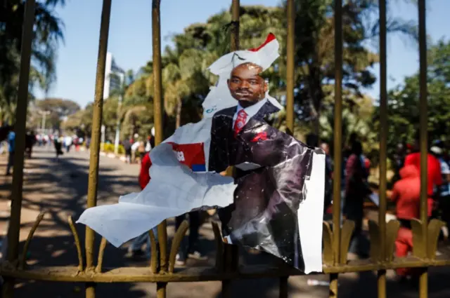 An election campaign poster of MDC Alliance leader Nelson Chamisa is left hanging by protestors at a gate after Zimbabwean police barricaded with water canons the entrance to the Rainbow Towers Hotel where the Zimbabwe Electoral Commission (ZEC) announced the results of the general election on August 1, 2018.