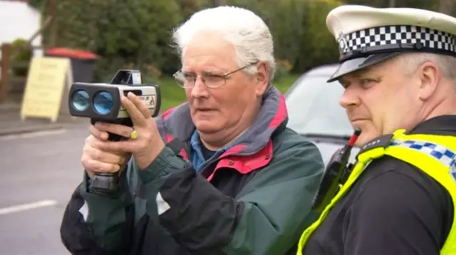 Man points speed gun under supervision from a police officer