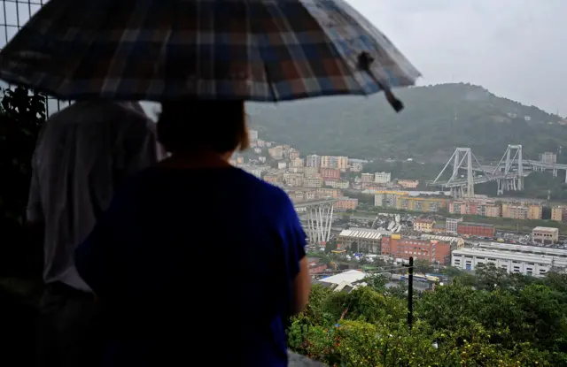 A couple, standing beneath an umbrella, look at the collapsed bridge