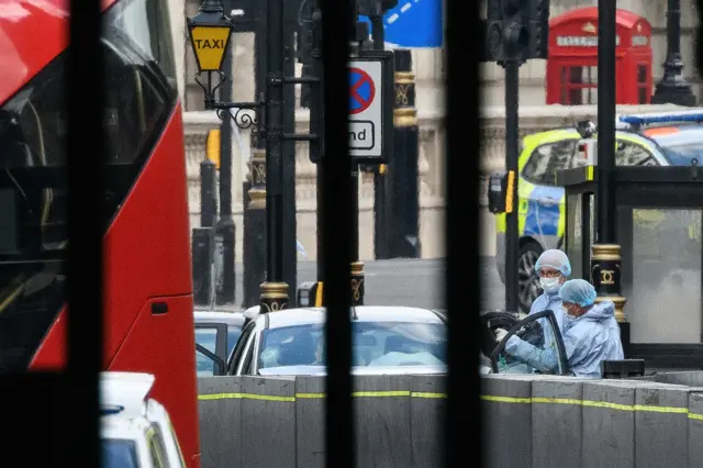 Forensic teams continue their work around a vehicle after it crashed into security barriers in Westminster