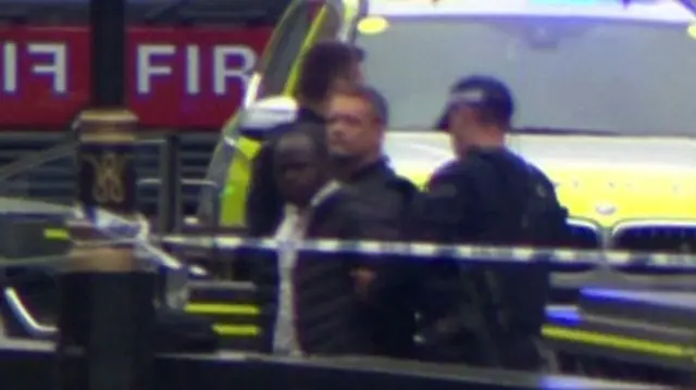 The suspect, in a black bomber jacket, being led away by police in London