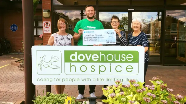 Four people stand behind Dove House sign, two of them are holding a large cheque