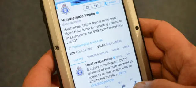 Hands hold a mobile phone showing a police twitter feed