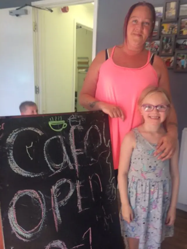 Cafe employee Sarah Staves and a young girl stand by a chalk board sign that says cafe open