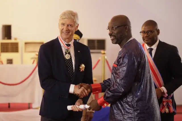 President, George Weah (C) decorates and inducts former soccer manager Arsene Wenger into the Order of Distinction and Knight Grand Commander of the Humane Order of African Redemption at the Samuel Kanyon Doe Sports Complex, Paynesville, outside Monrovia, Liberia, 2