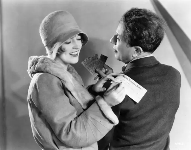 circa 1920: A smiling Marion Davies signs a cheque on Sid Grauman's shoulder for tickets to 'The Broadway Melody'.