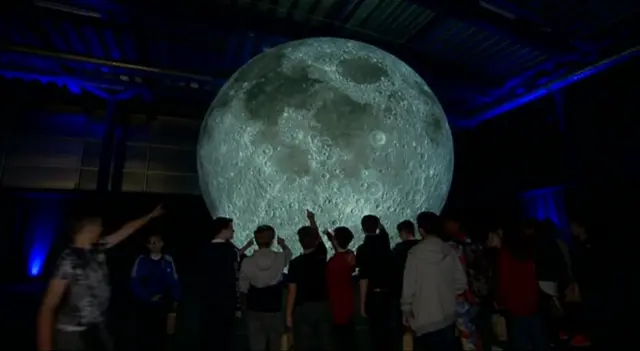 A group of young people look at the moon artwork