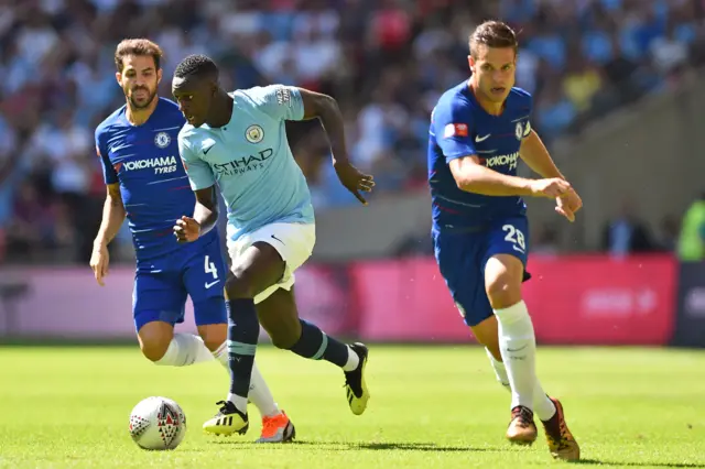 Benjamin Mendy (C) runs between Chelsea"s Spanish midfielder Cesc Fabregas (L) and Chelsea"s Spanish defender Cesar Azpilicueta