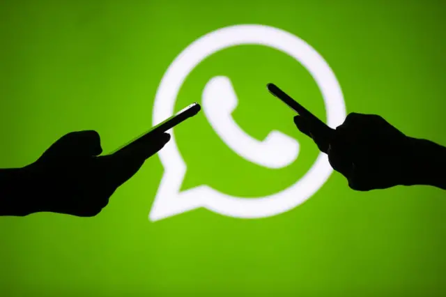 People hold mobile phones in front of the logo of WhatsApp application