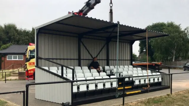 Lorry and crane lowering the stand onto the edge of the pitch.