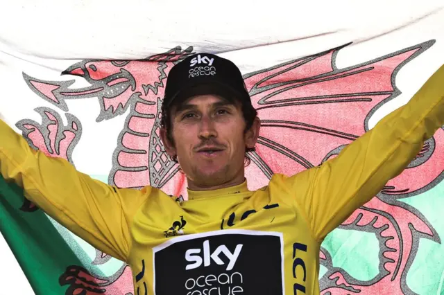 Geraint Thomas wearing the yellow jersey and holding the Welsh flag