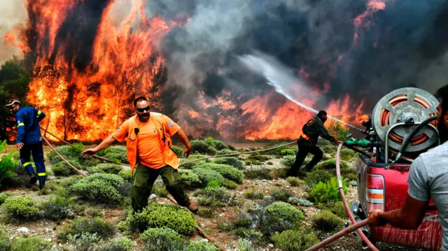 Firefighters and volunteers try to extinguish flames during a wildfire at the village of Kineta, near Athens