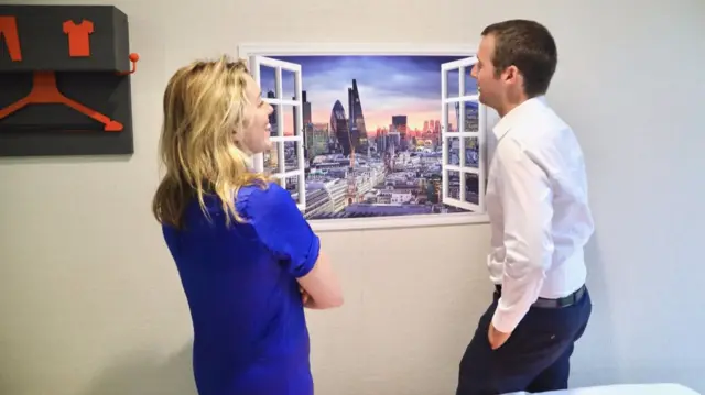 Two members of staff look out of a fake window