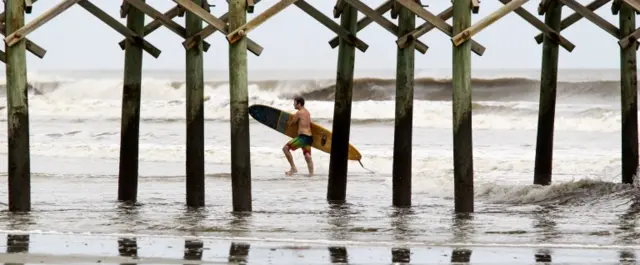 Man carries surfboard on beach amid waves