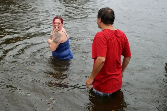 People walk in flooded streets as the Neuse River begins to flood its banks