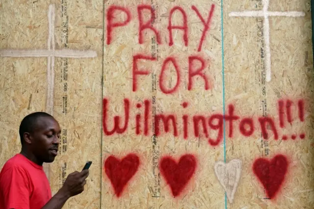 Boarded up house with spray painted text: Prayers for Wilmington