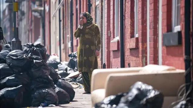 A woman in Birmingham surrounded by uncollected rubbish