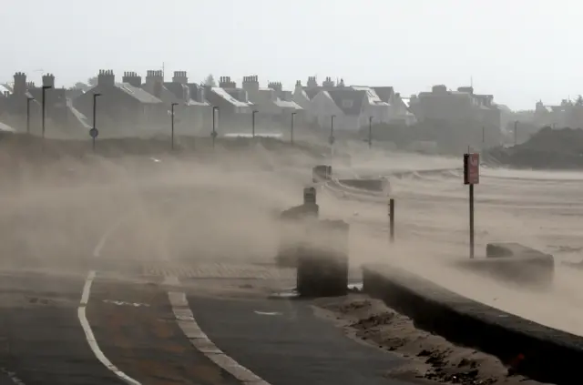 High winds drive sand and sea spray across the street at Troon beach