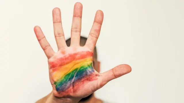 A man holding up his hand with an LGBT flag painted on his palm