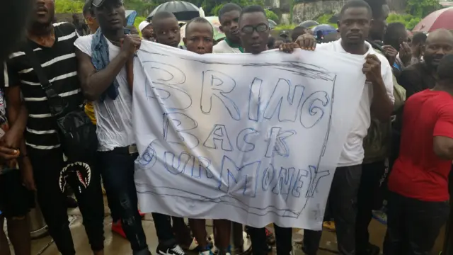 Protesters hold a sign reading "bring back our money"