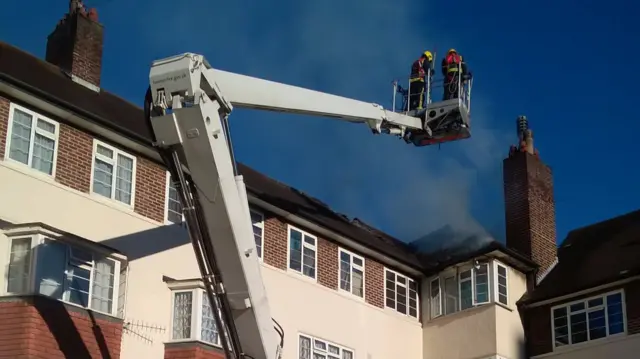 Firefighters on a crane by the smoking building