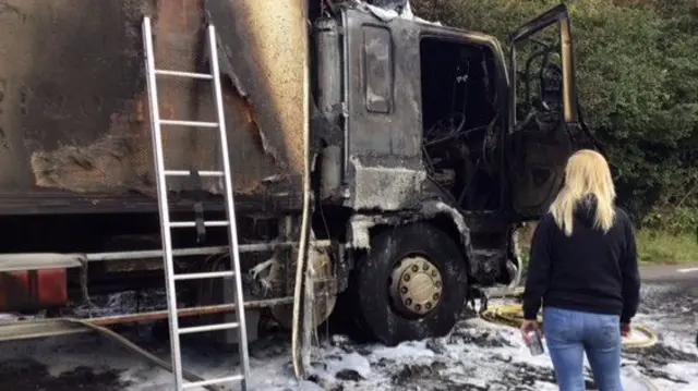 Woman next to burnt out lorry