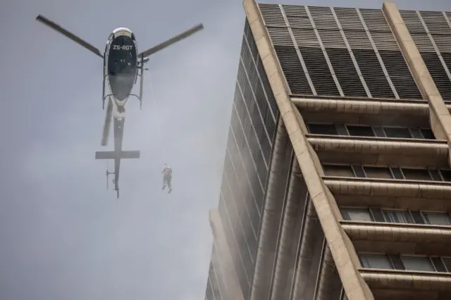 A South African Police Service helicopter rescues a trapped firefighter from a building on fire in the Central Business District of Johannesburg on September 5, 2018