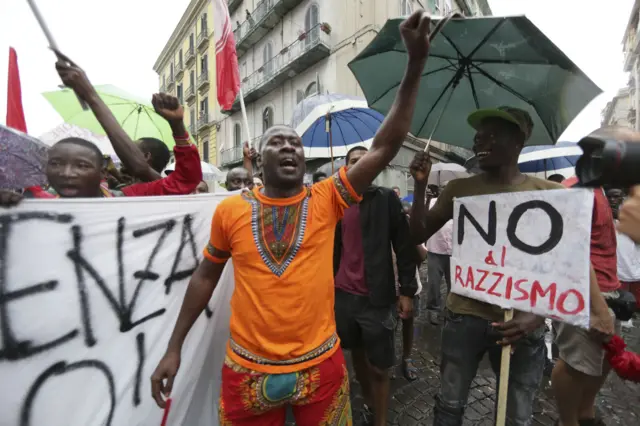 Demonstrators hold banners and shout slogans against racism during a rally in solidarity with a migrant from Senegal wounded by pistol shot in the centre of Naples