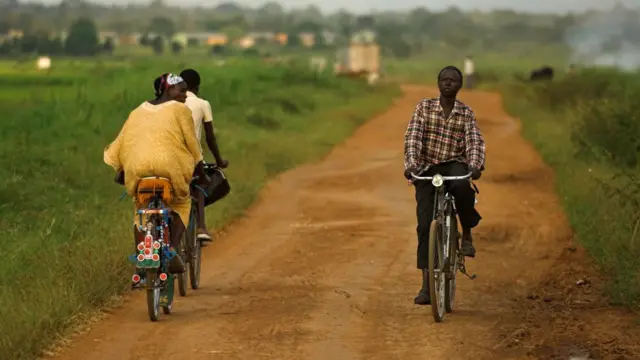 Cyclists cycling on path surrounded by fields of crops, near Mbale, Uganda