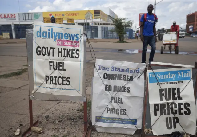 Members of the public walk past newspaper placards