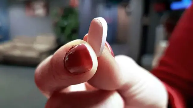 A woman holds an oval-shaped pill in her hand