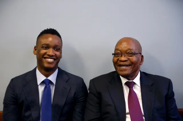 Duduzane Zuma shares a laugh with his father, former South African president Jacob Zuma, ahead of Duduzane"s appearance at the Specialised Commercial Crimes Court in Johannesburg