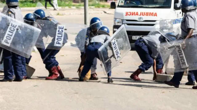 Police officers make way for an ambulance by removing stones from a barricade during a 'stay-away' demonstration against the doubling of fuel prices