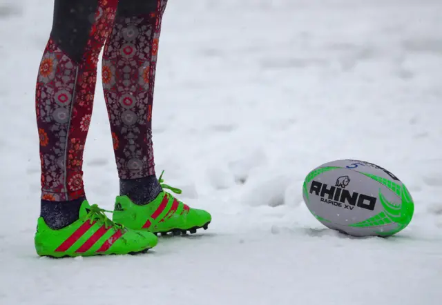 A person standing in rugby boots with a rugby ball in the snow