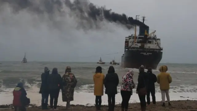 people standing on a beach looking at a ship grounded a few metres from the shore